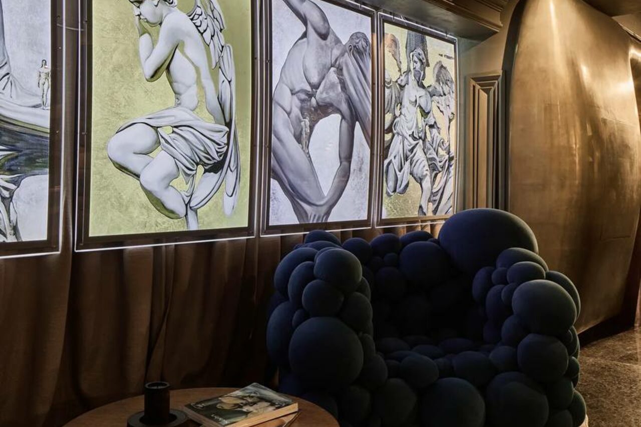 Арендовать Communitymoscow (Коммьюнити Москоу).Зал Библиотека. Многофкнкциональное пространство. Тёмное помещение с креслом необычной формы, состоящим из мягких шаров. На стене панно с изображениями статуй. Освещение мягкое, стены и пол выполнены в тёмных тонах. Рядом с креслом круглый столик с книгами.