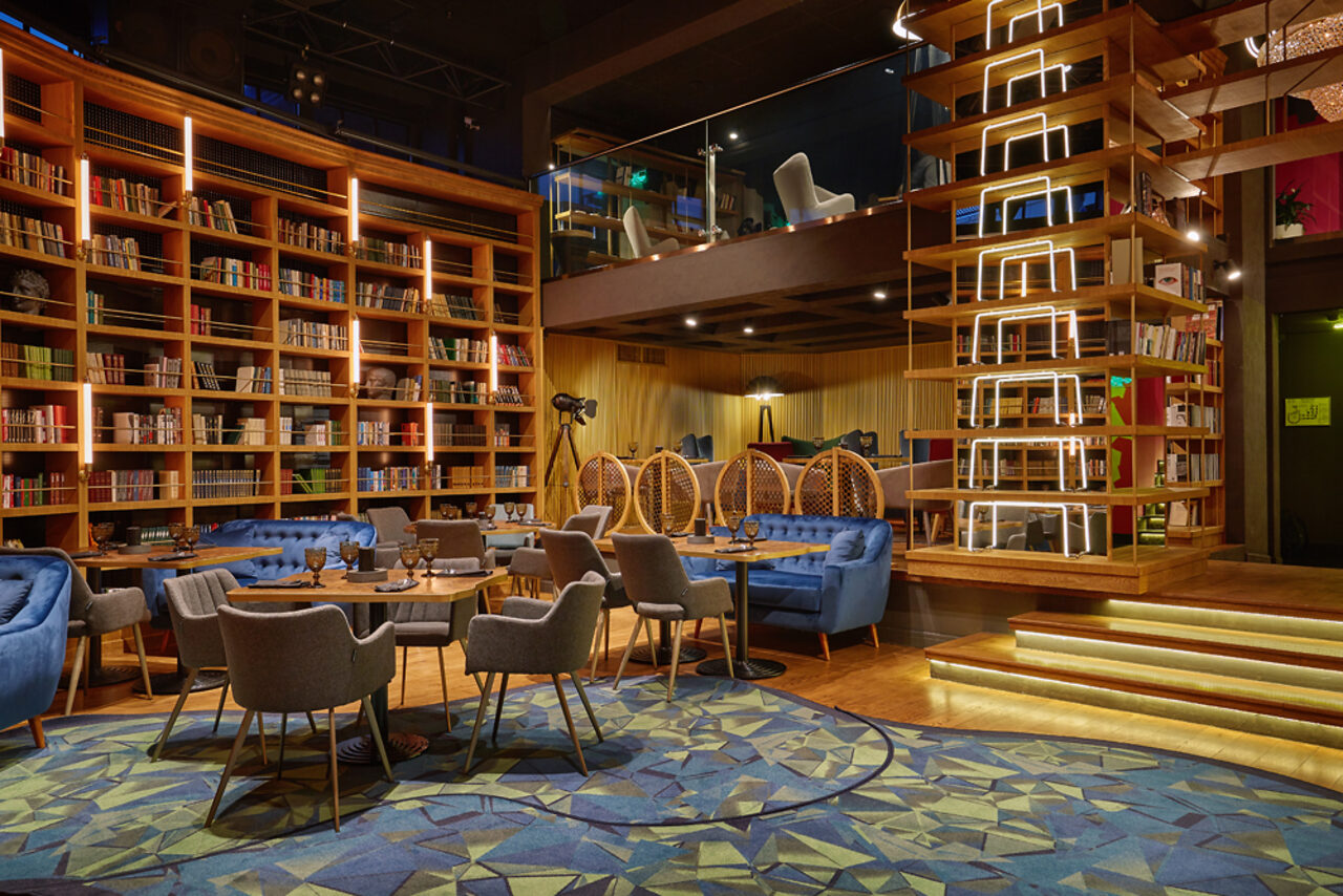 Арендовать Communitymoscow (Коммьюнити Москоу).Зал Библиотека. Многофкнкциональное пространство. Библиотечное пространство с книжными стеллажами, синими диванами и креслами, круглые столы. На втором уровне также кресла, подвесные кресла, открытая лестница со светодиодной подсветкой. Деревянные и металлические конструкции, яркое искусственное освещение.