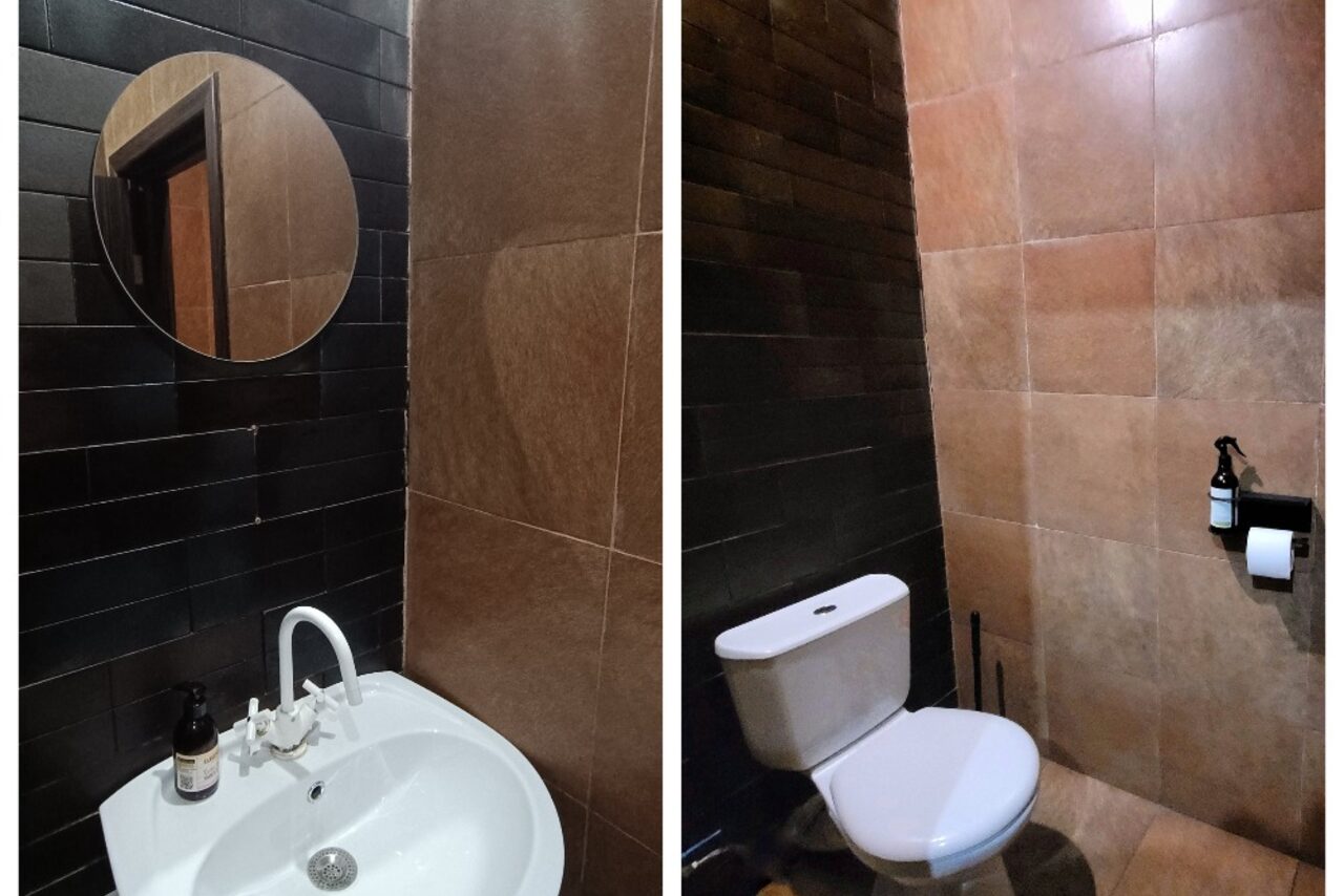 Арендовать Элегантный лофт с хорошим звуком и балконом. Санузел с раковиной и унитазом. Черная и коричневая плитка на стенах. Круглое зеркало над раковиной, белый кран и бутылка с жидкостью. Держатель для туалетной бумаги с рулоном.