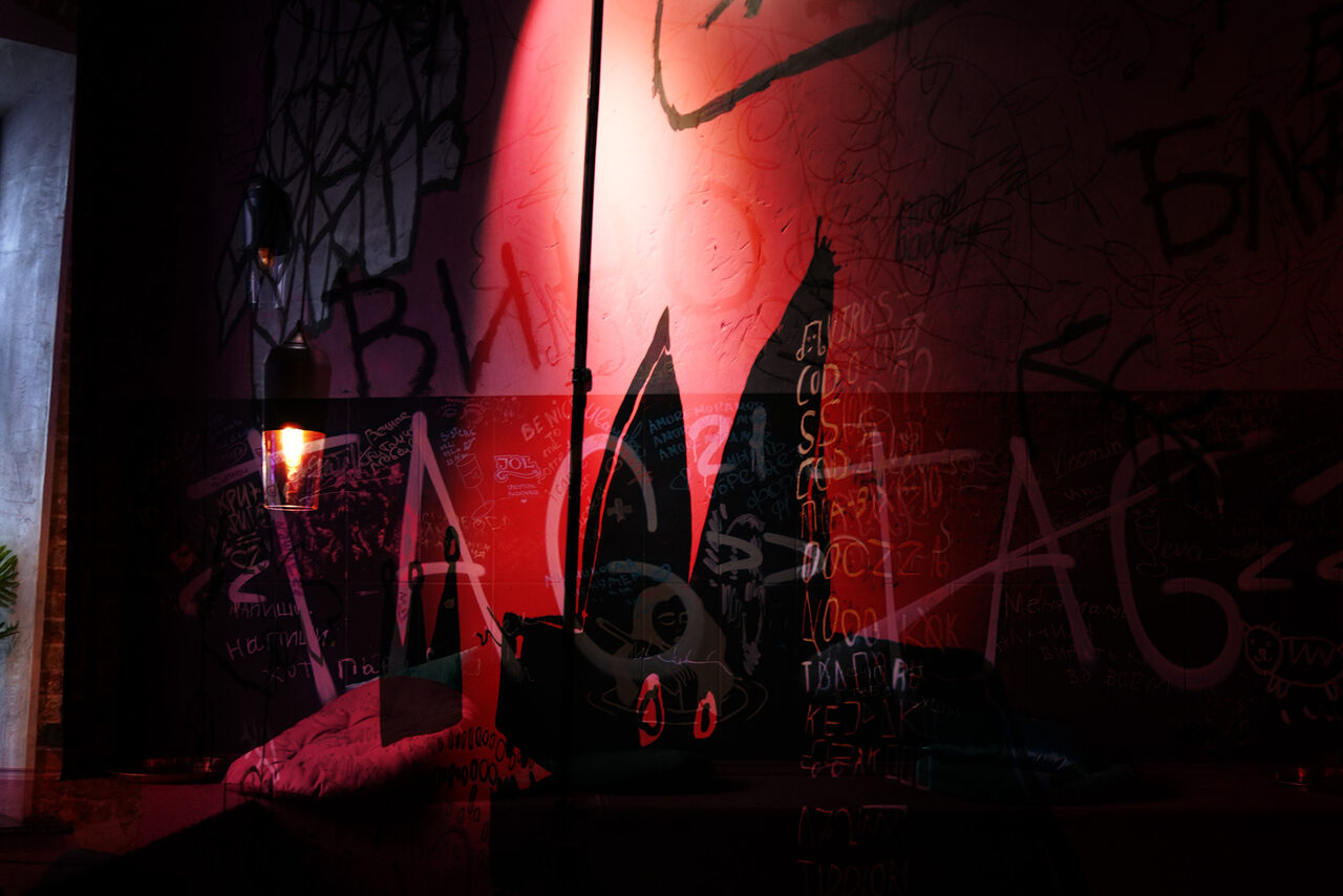 Арендовать Винный бар “Дело не в вине”. Креативное пространство с граффити на стенах, декоративный светильник с теплым освещением, мягкая мебель. Темные и насыщенные цвета, присутствует настенное искусство и текст в виде граффити.