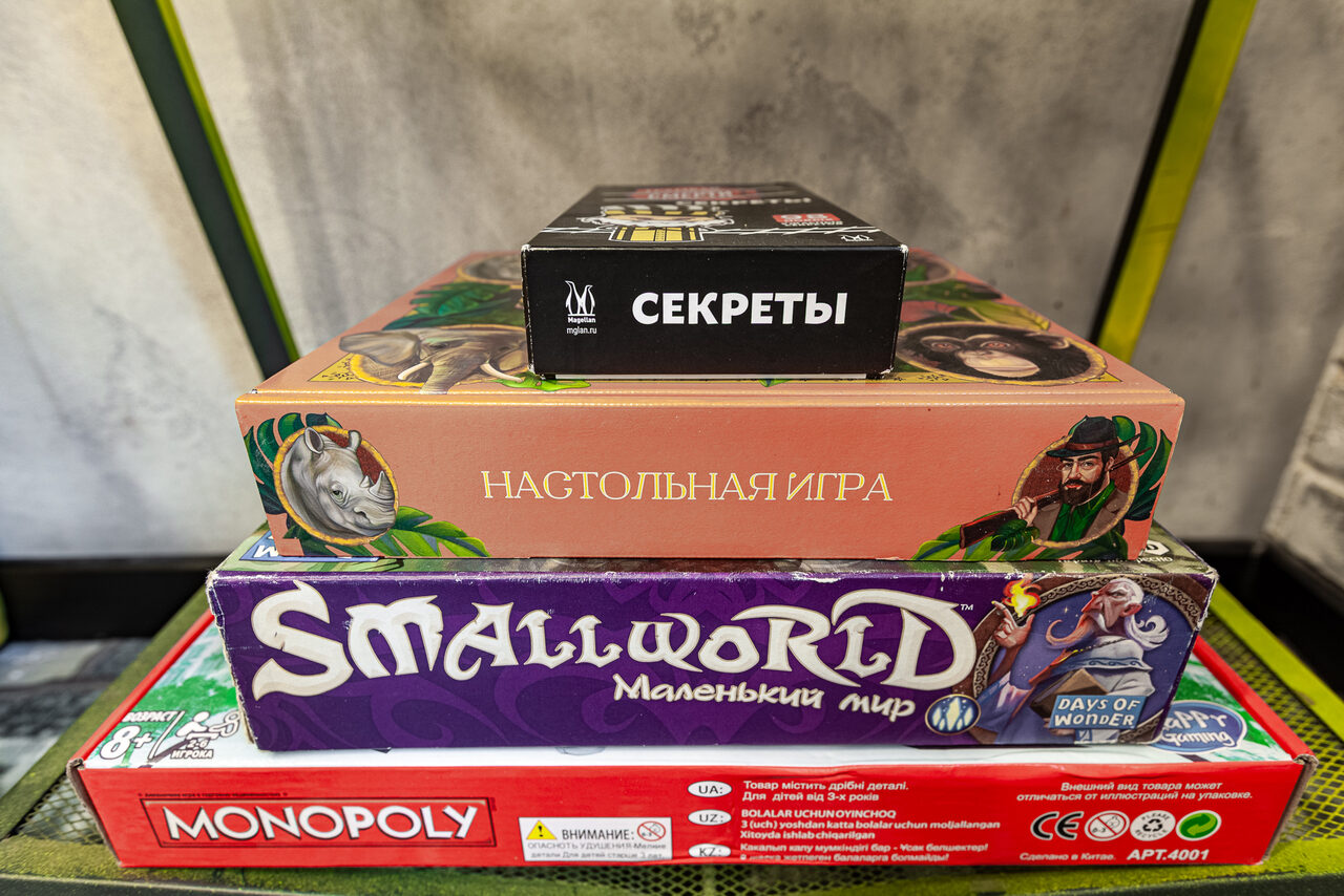 Арендовать Лофт где можно все. Стопка настольных игр на фоне серой стены. Включает в себя игры с названиями: "Секреты", "Настольная игра" с иллюстрацией животных, "Small World Маленький мир", "Monopoly".
