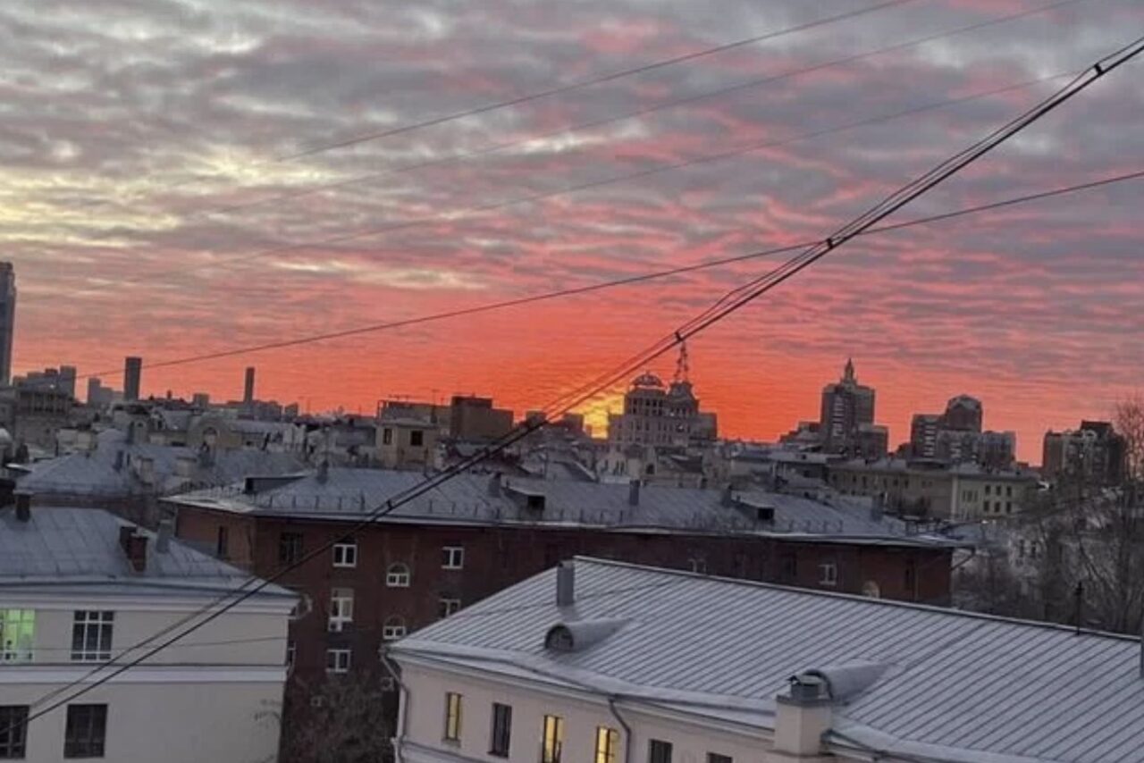 Арендовать Лофт где можно все. Вид на городские крыши на фоне заката. Небо покрыто облаками с оранжевым и розовым оттенками. В кадре несколько жилых зданий, городские линии электропередач.