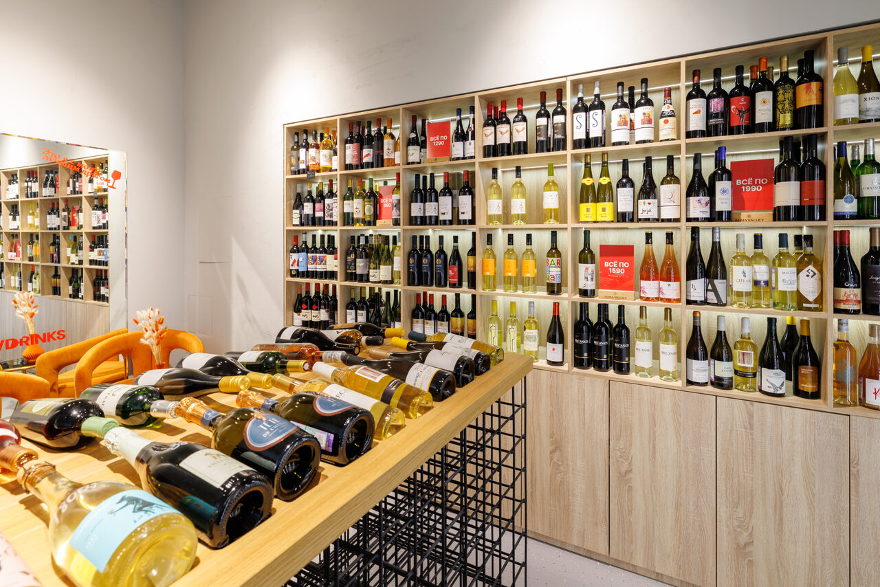 Арендовать Винотека AVDRINKS(АВДРИНКС) на 12 гостей. Помещение с настенными полками, заполненными бутылками вина. В центре деревянный стол с сетчатым основанием, на котором выставлены бутылки. Стены светлые, освещение яркое. На заднем фоне зеркала.
