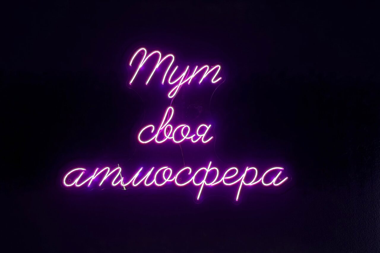Арендовать Лофт «Блэкберри». Неоновая надпись на тёмном фоне: "Тут своя атмосфера". Цвет - фиолетовый.