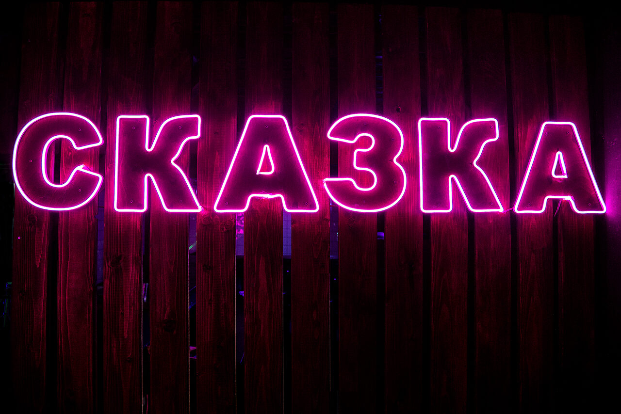 Арендовать СКАЗКА - неоновый лофт с джакузи! Лучший сервис, лед и приставка в подарок. Неоновая вывеска с надписью "СКАЗКА" на фоне деревянной стены. Цвет подсветки — розовый.