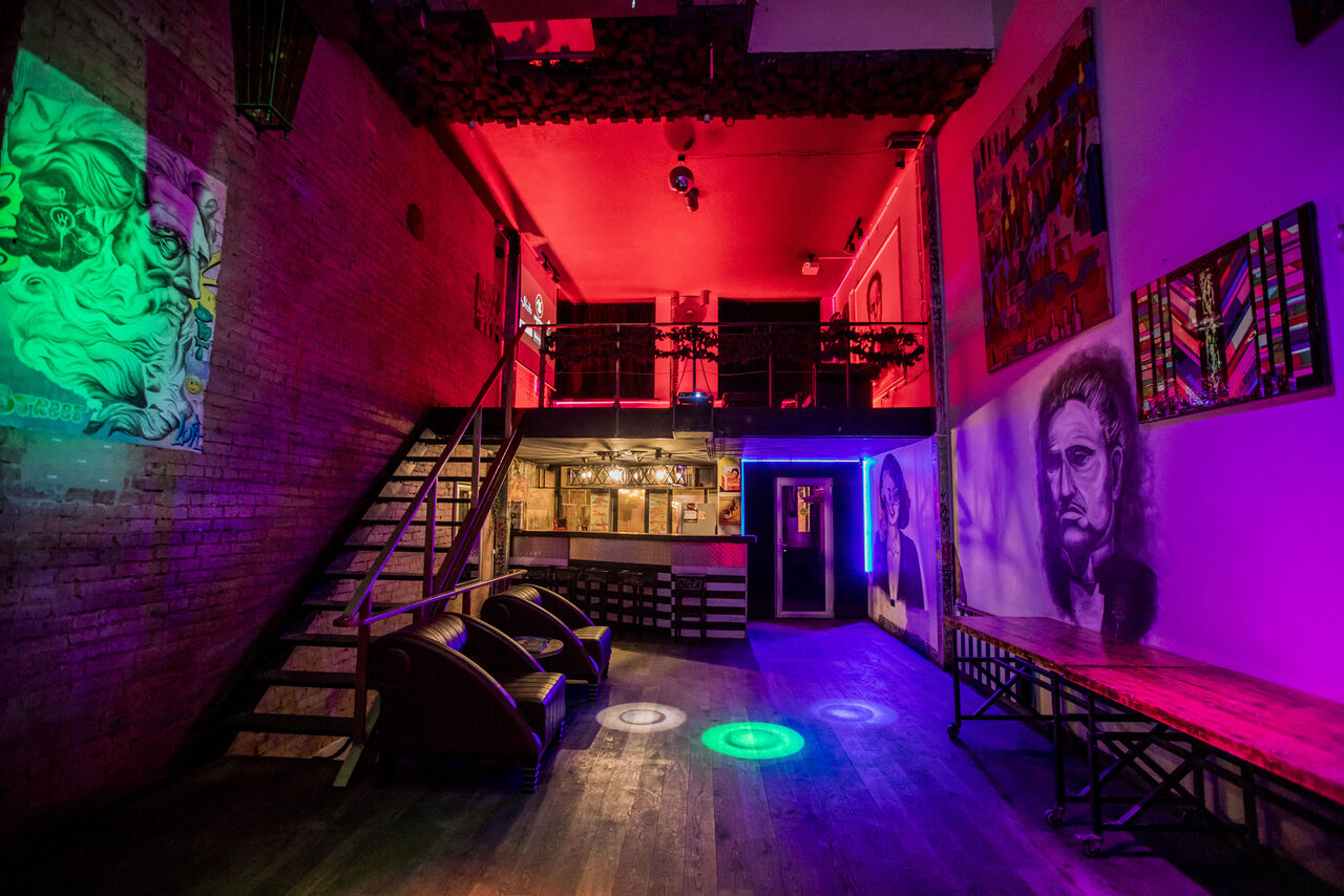 Арендовать Street Art Loft (Стрит Арт Лофт). Лофт с кирпичными стенами, деревянным полом и открытым потолком. Мезонин с металлическими перилами. Два кресла, длинная деревянная скамья, светильники, разноцветное освещение. На стенах красочные рисунки. Ступени из дерева и металла.