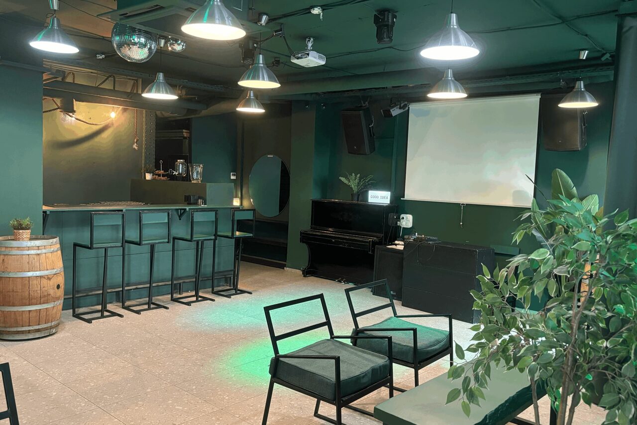 Арендовать Work Shop Loft(Воркшоп Лофт). Зал 11 . Лофт-пространство с баром, барные стулья, диваны, экран, пианино, деревянная бочка, зелёные стены, потолочные светильники, растительность в горшках, подвесные светильники.
