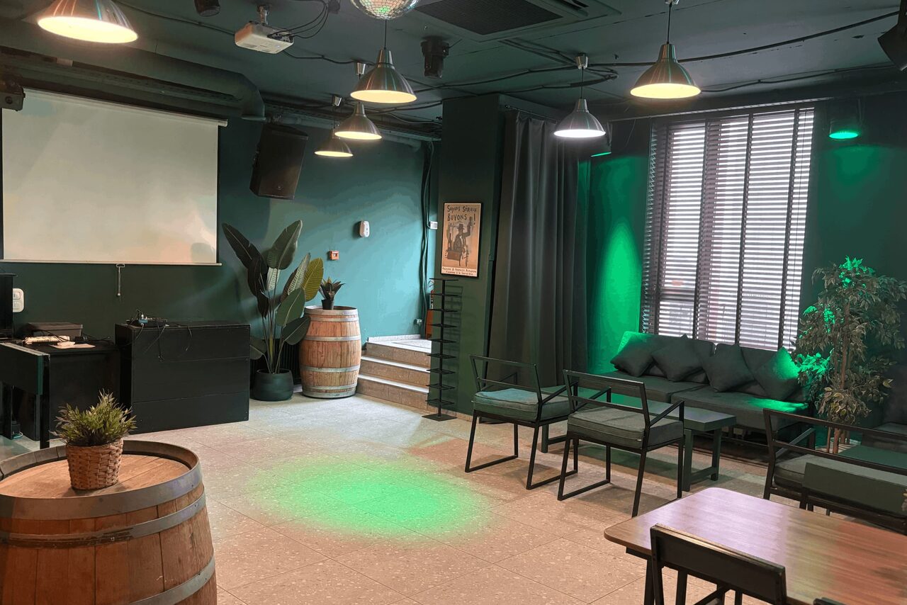 Арендовать Work Shop Loft(Воркшоп Лофт). Зал 11 . Многофункциональное пространство с проектором и экраном, деревянные бочки, диваны и столы. Стены и потолок тёмно-зелёного цвета. Лампы подвесные, окна с жалюзи. Есть декоративные растения и картина на стене.