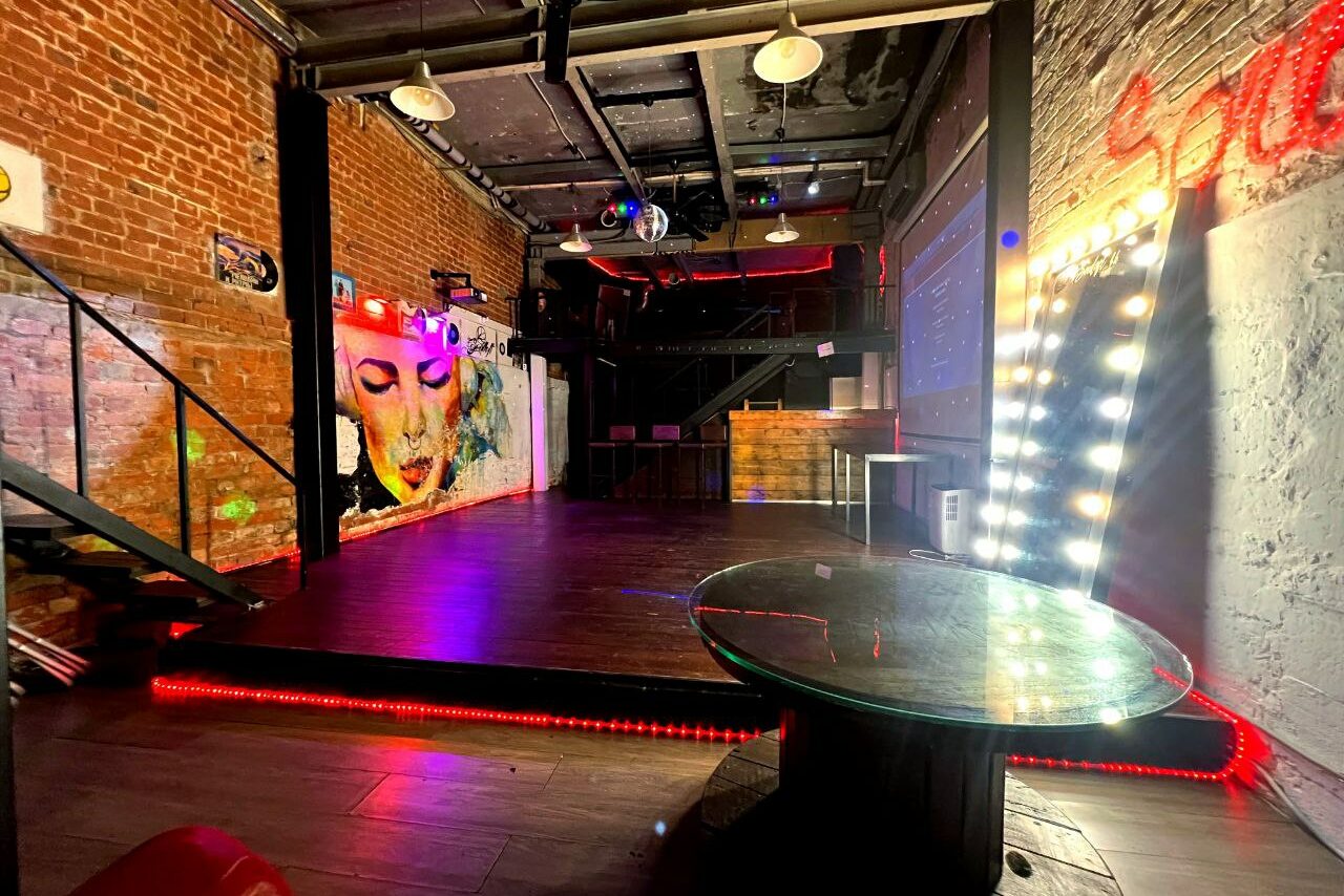 Арендовать Soul Loft . Крупный план угла большого зеркала и гирлянд на ней, всё расположено у кирпичной стены