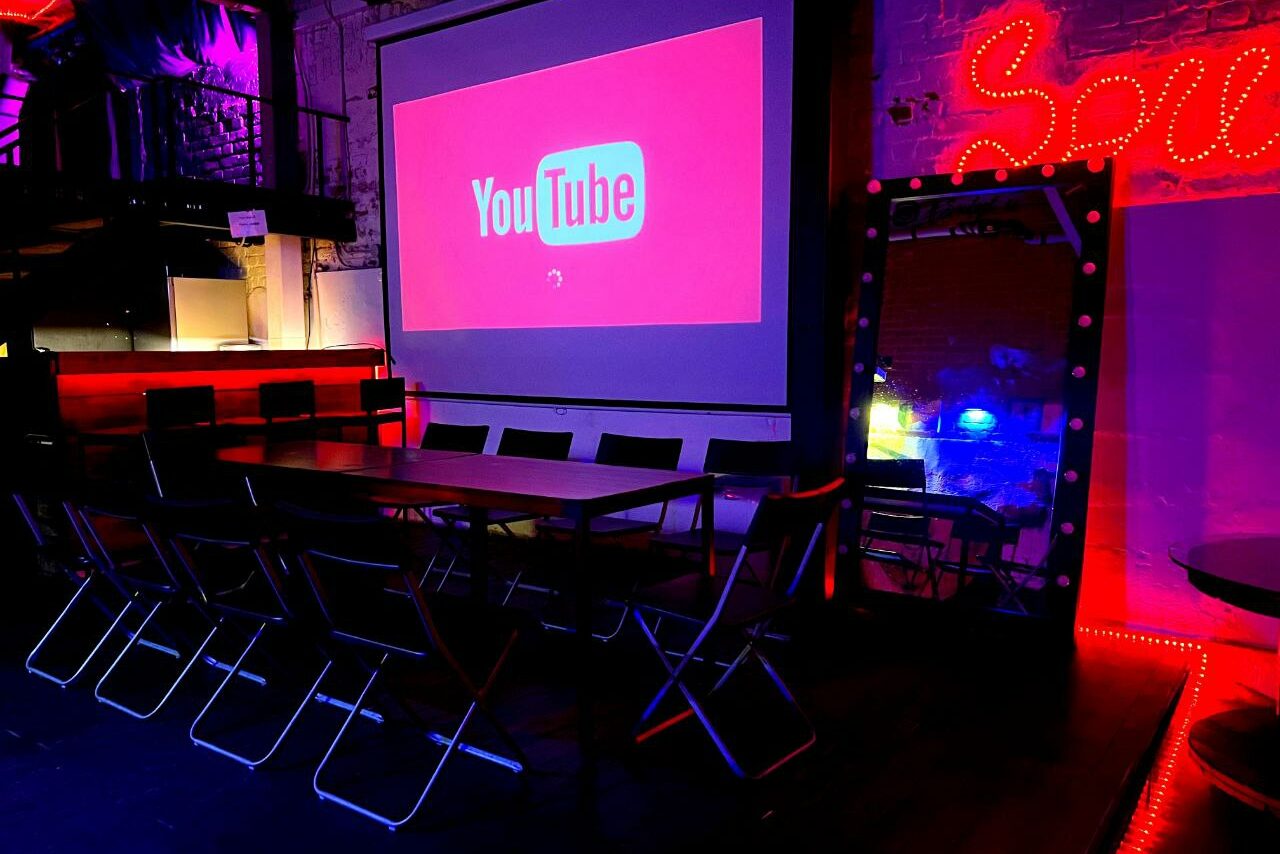 Арендовать Soul Loft . Изображён зал в лофте с ракурса второго этажа. Видно обрисованную стену, рядом со стеной стоят столы и стулья 