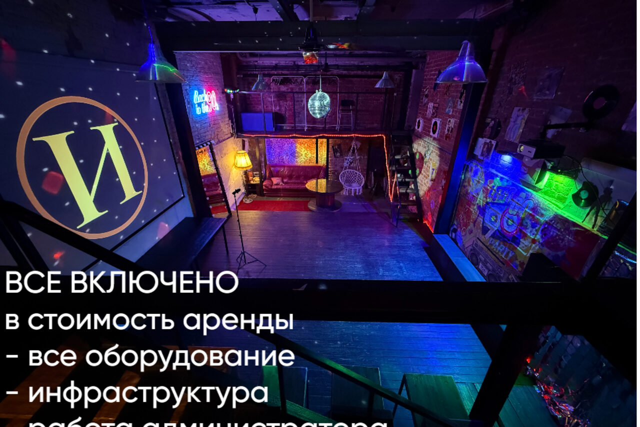 Арендовать Лофт ИЗНАНКА. Зал ЛИХИЕ 90-е. Затемнённая комната лофта, много людей в кадре проводят фуршетное мероприятие, беря еду с объединённых столов. Несколько людей на кадре танцуют