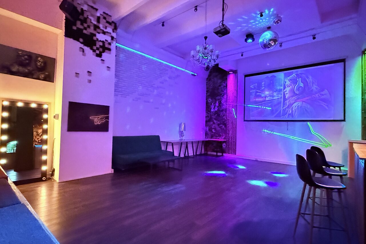 Арендовать Bar on Presnya for private events. Многофункциональное пространство с белыми кирпичными стенами и деревянным полом, оснащенное проектором, стульями, диваном и гримерным зеркалом. Современное освещение с элементами неона, диско-шар на потолке, абстрактное искусство на стенах.