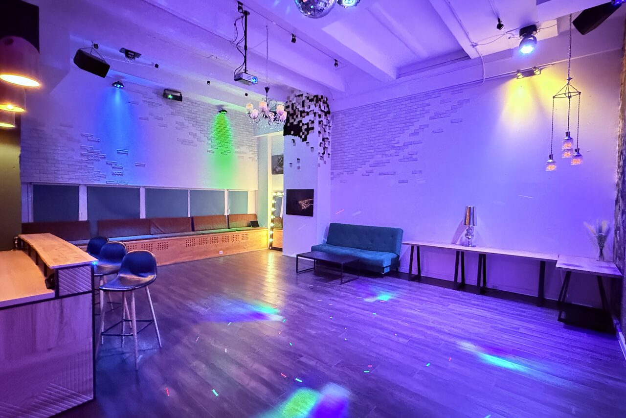 Арендовать Bar on Presnya for private events. Просторное помещение с барной стойкой и высокими стульями, диванами вдоль стены, столами и скамьями. Освещение разноцветное, свет от прожекторов. Потолок белый, стены с узором из белых и светлых кирпичей. Пол темный, деревянный.