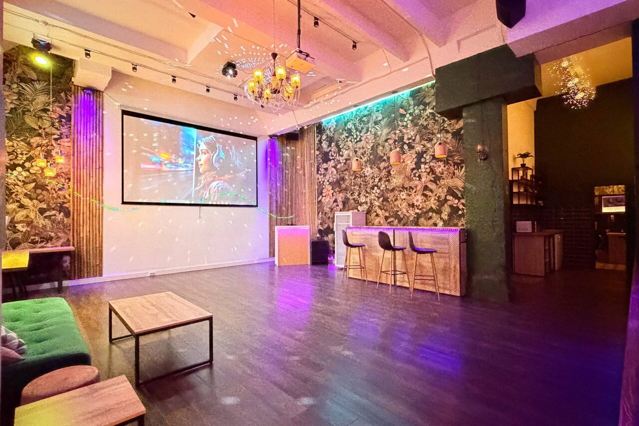 Арендовать Bar on Presnya for private events. Просторное помещение с темным деревянным полом и декоративными стенами с цветочным узором. В углу большой экран, рядом барная стойка с высокими стульями. Мягкий диван, низкий столик. Освещение состоит из подвесных светильников и встроенных ламп.