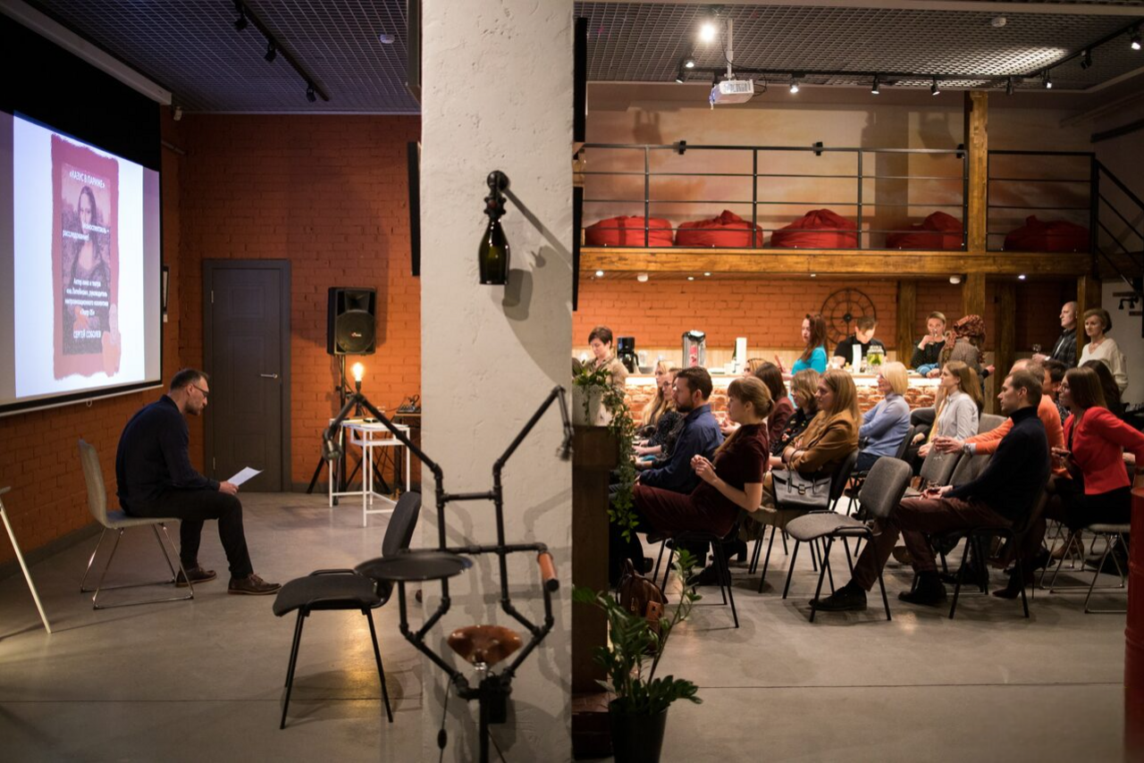 Арендовать Стильный двухуровневый лофт. Человек ведёт лекцию. Слушатели смотрят на экран и лектора