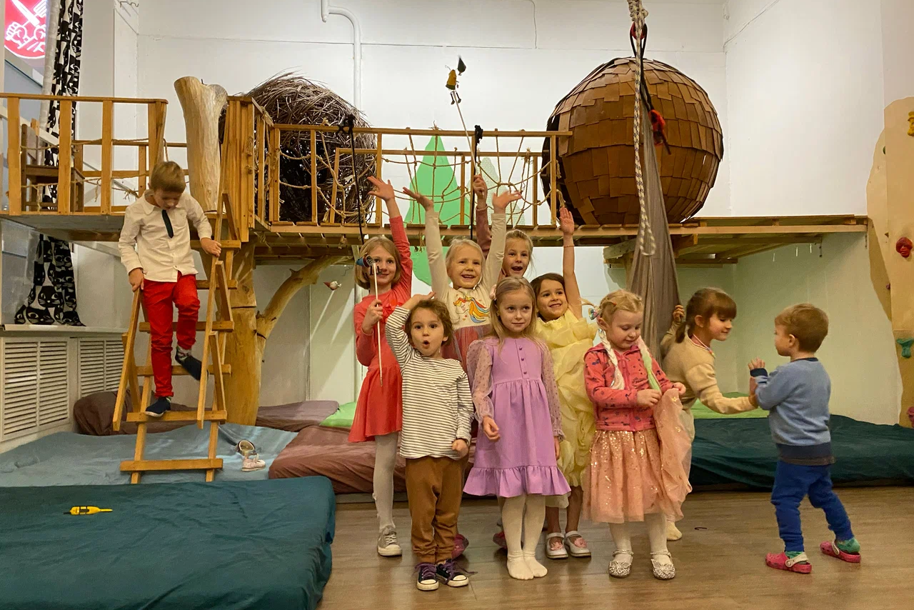 Арендовать Children's eco-loft. Детская игровая комната с деревянными конструкциями, подвесным мостом, лестницей и воздушными шарами. Мягкие матрасы на полу. Светлые стены, разноцветная одежда у детей. Помещение хорошо освещено.
