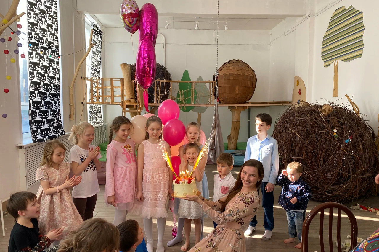 Арендовать Children's eco-loft. Детская игровая комната с деревянными конструкциями для лазания, украшена шарами и наклейками в виде деревьев. Светлые стены, деревянный пол. Большие окна с занавесками, много детей, взрослый с тортом.