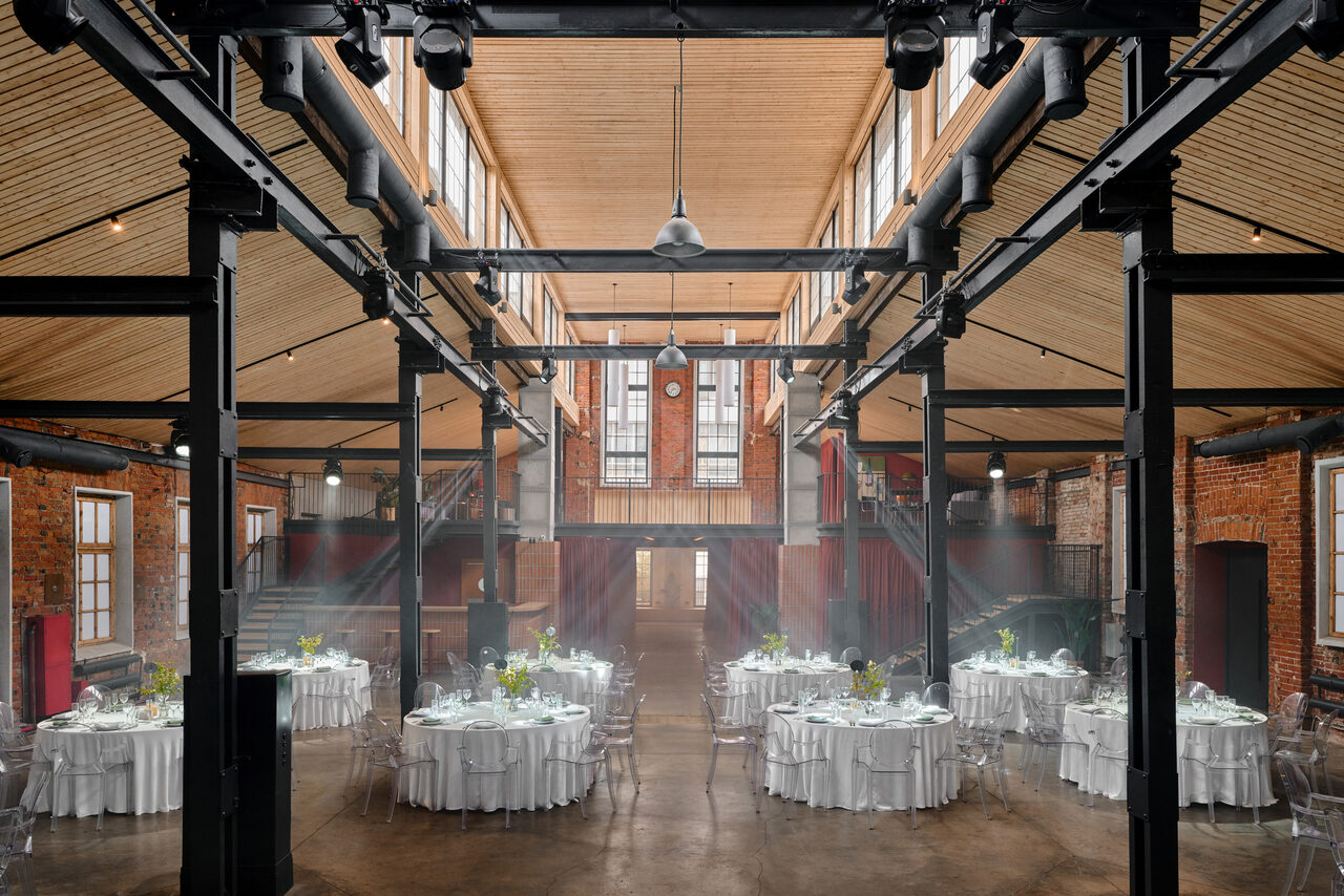 Арендовать AG Loft. Urban (АГ Лофт. Урбан). Просторный лофт с раритетным автомобилем. Большое открытое пространство промышленного типа с высокими потолками и деревянной отделкой. Красные кирпичные стены. Круглые столы с белыми скатертями и прозрачными стульями. Верхнее освещение, окна вдоль потолка. Стальные балки и колонны.
