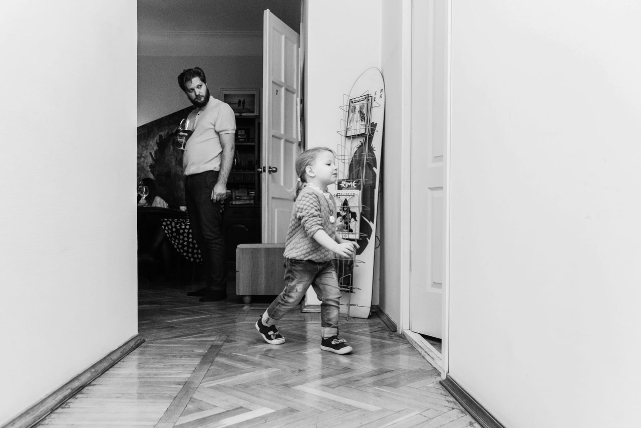 Арендовать Светлый лофт с панорамным видом. Чёрно-белая фотография. Ребёнок бежит из одной комнаты в другую. На заднем плане стоит мужчина