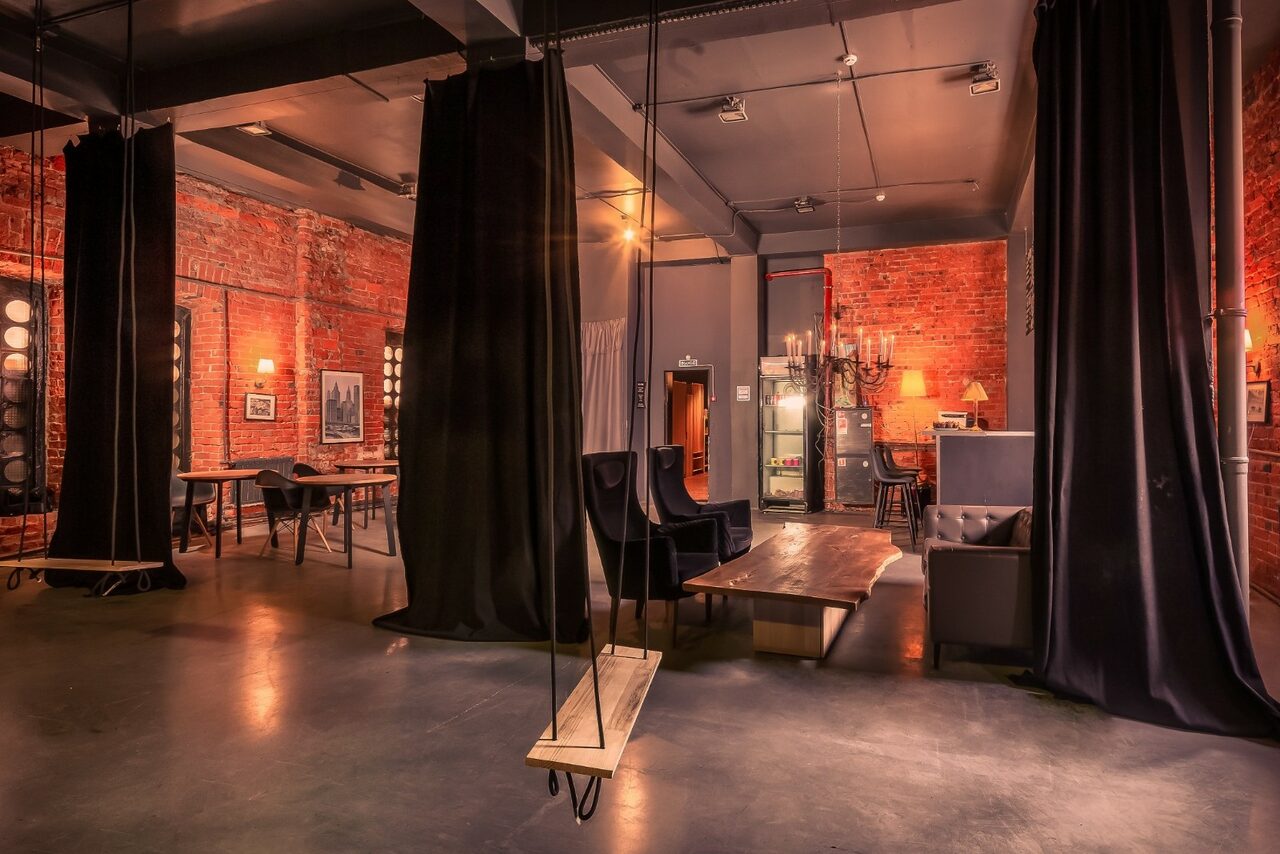 Арендовать Music loft (Мьюзик лофт). Лофт-пространство с кирпичными стенами и бетонным полом, планировка открытая. В помещении есть качели на цепях, столы и стулья, мягкие диваны. Освещение точечное, на стенах фотографии. Занавески разделяют пространство.