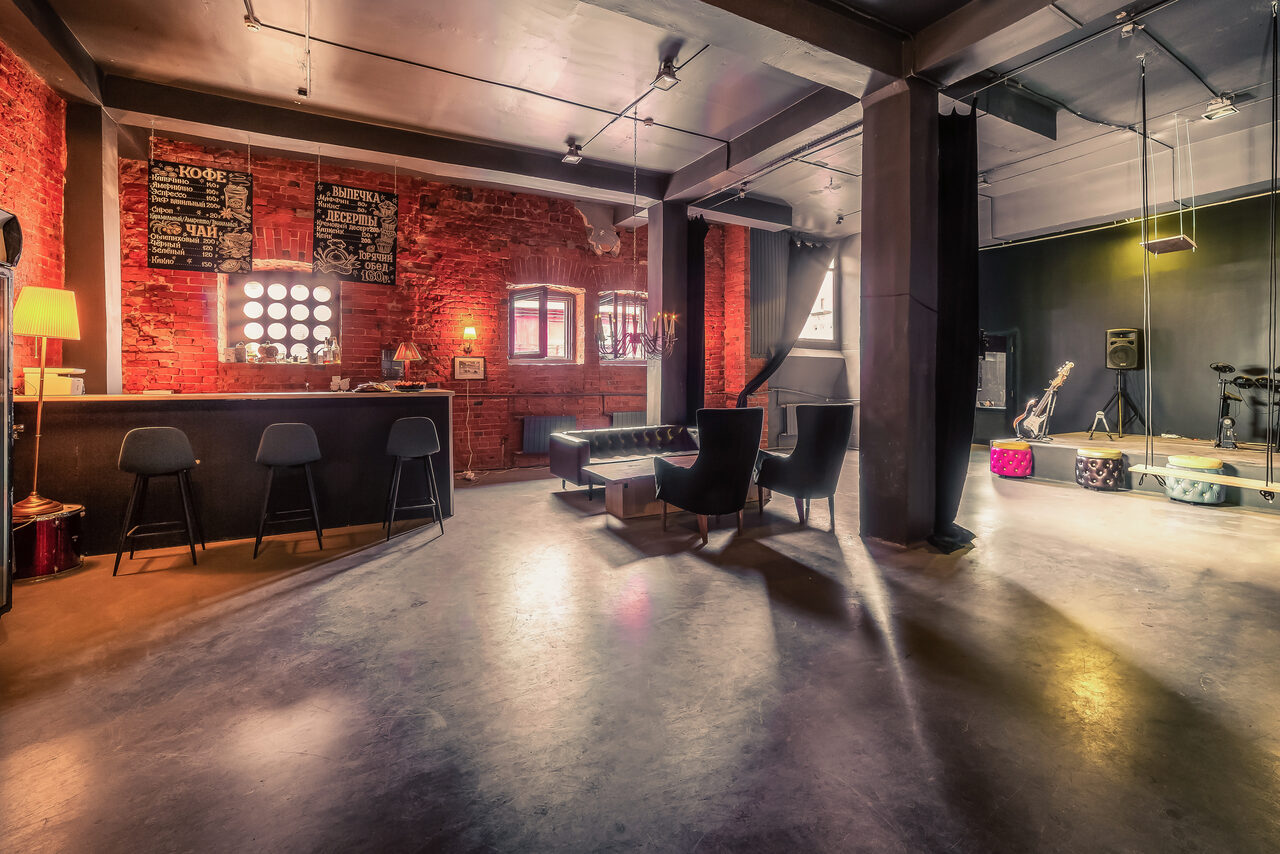 Арендовать Music loft (Мьюзик лофт). Лофт-пространство с кирпичными стенами, барной стойкой и высокими потолками. Черные стулья, кожаные диваны, музыкальная аппаратура, светильники, несколько окон. Основные цвета: красный, черный, серый. Таблички на стене, гладкий пол.